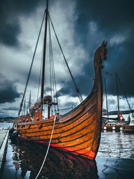Holzboot mit Drachenkopf an einem Steg im Wasser, umgeben von dunklen Wolken
