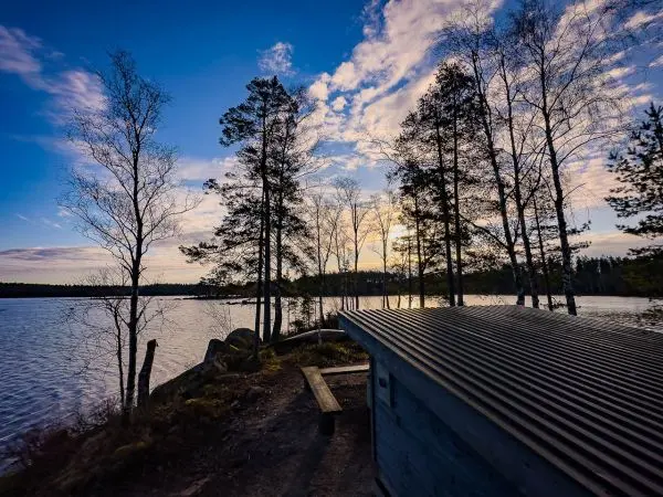 Holzhütte mit Blechdach am Ufer eines Sees, umgeben von Bäumen