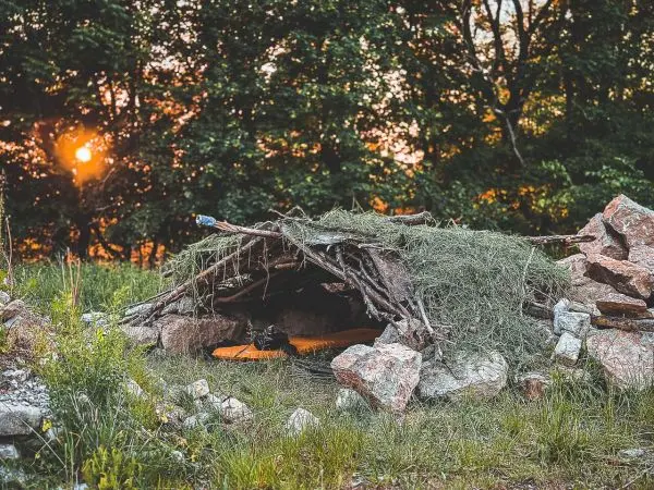 Laubhütte aus Ästen und Steinen mit Grasabdeckung im Sonnenuntergang