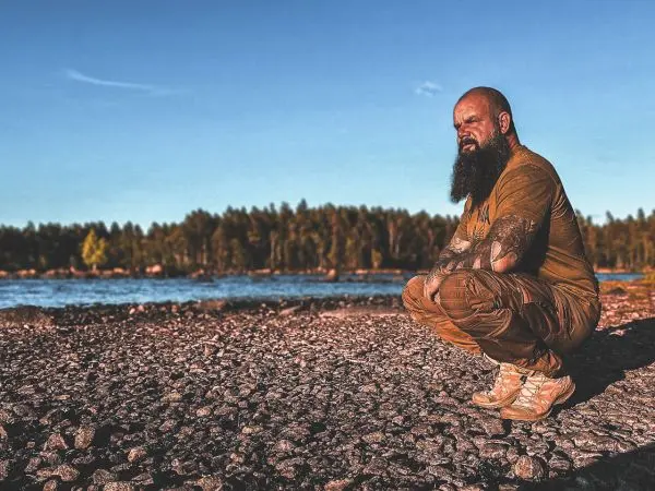 Mann hockt auf Kiesstrand und schaut nachdenklich auf den See