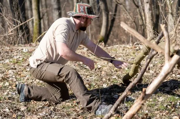 Mann kniet und schneidet mit einem Messer einen Ast im Wald