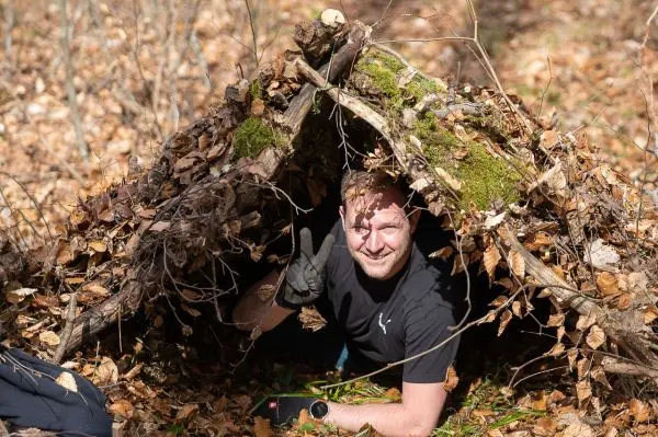 Mann zeigt Peace-Zeichen aus einer Laubhütte mit Zweigen und Blättern