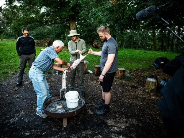 Mann zerlegt einen gefangenen Fisch über einem Feuergrill, während andere zuschauen