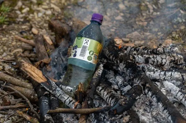 Plastikflasche steht in einem Haufen glühender Holzreste