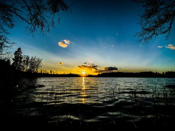 Sonnenuntergang über einem ruhigen See mit Wolken und Bäumen