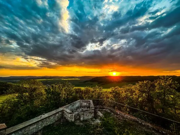 Sonnenuntergang über einer Landschaft mit Bäumen und Wolken