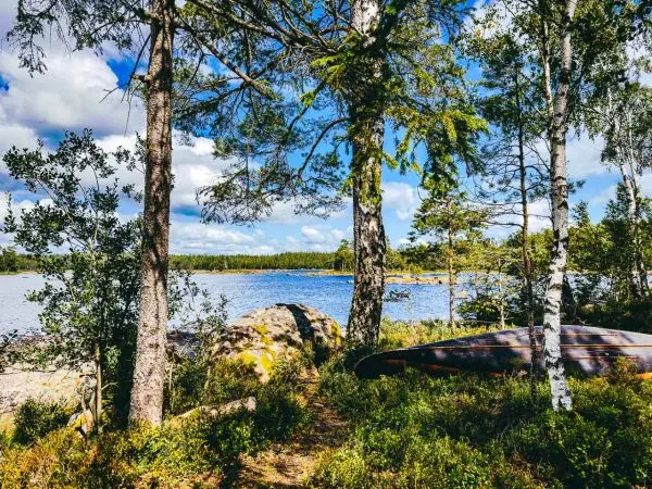 Uferbereich mit Bäumen, Steinen und einem Kanu am Wasser