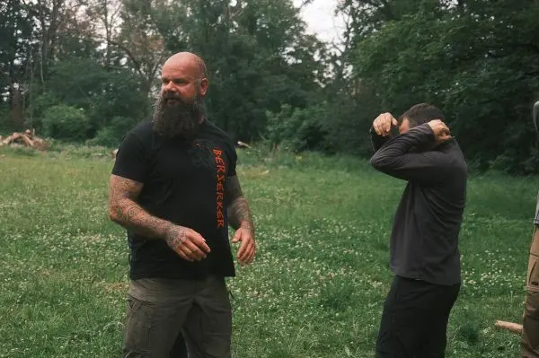 Zwei Männer stehen in einer Wiese, einer zieht sich ein Oberteil über