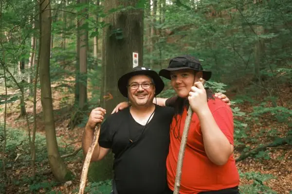 Zwei Personen mit Wanderstöcken stehen im Wald vor einem Baum