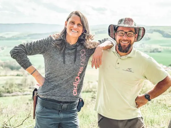 Zwei Personen stehen lächelnd nebeneinander, im Hintergrund eine grüne Landschaft