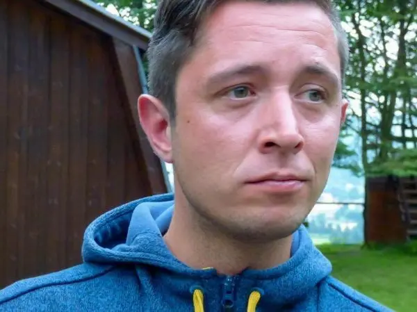 Ein Mann mit blauer Jacke steht vor einer Holzstruktur im Freien