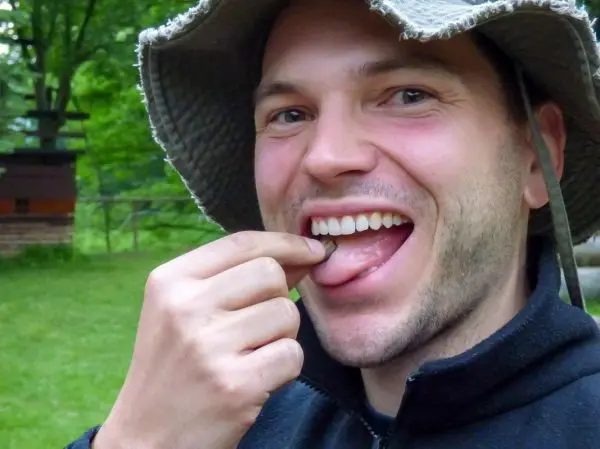 Mann hält einen kleinen Gegenstand zwischen Daumen und Zeigefinger vor den Mund