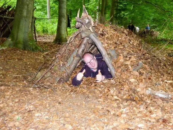 Mann liegt in einer selbstgebauten Laubhütte aus Ästen und Blättern