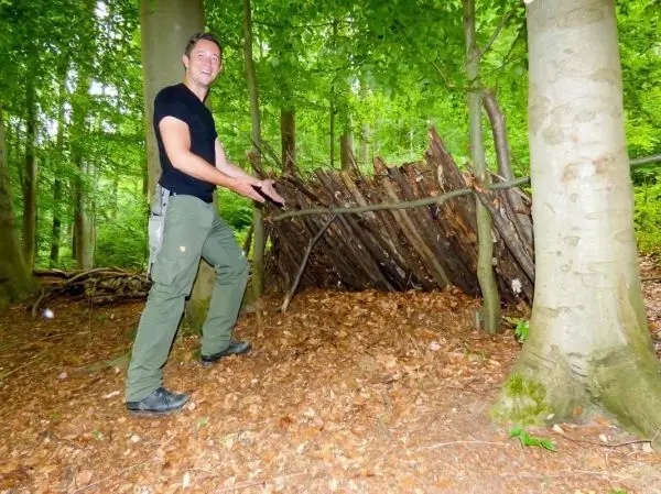 Mann präsentiert eine selbstgebaute Laubhütte aus Ästen im Wald