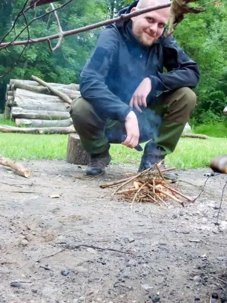 Person sitzt neben einem kleinen Feuer aus Ästen