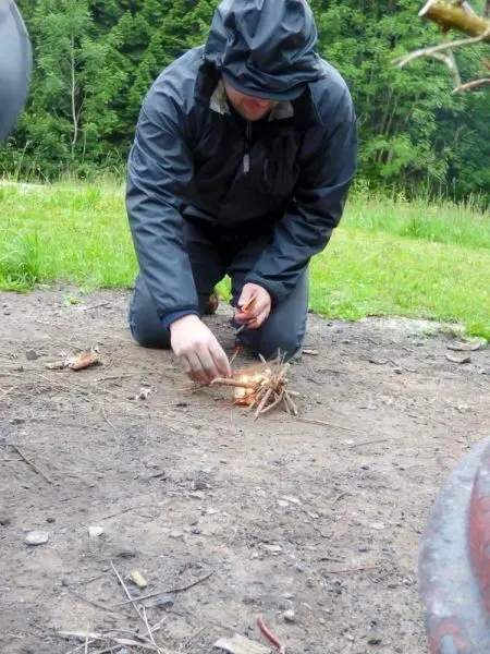 Person zündet kleine Feuerstelle mit Zweigen an beim Überlebenstraining