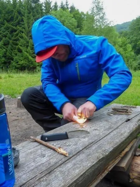 Person zündet mit einem Feuerstein Holz auf einem Tisch an beim Survival Training