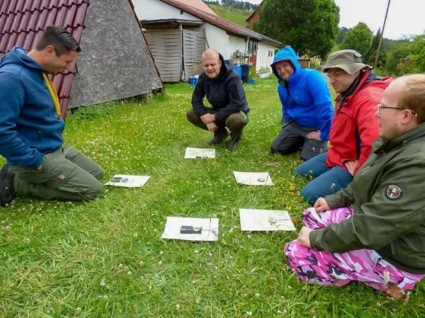Sechs Personen sitzen im Gras und betrachten Karten auf dem Boden