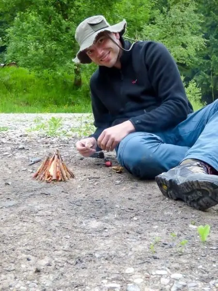 Zunder wird neben einem kleinen Feuer mit einem Feuerstahl entzündet
