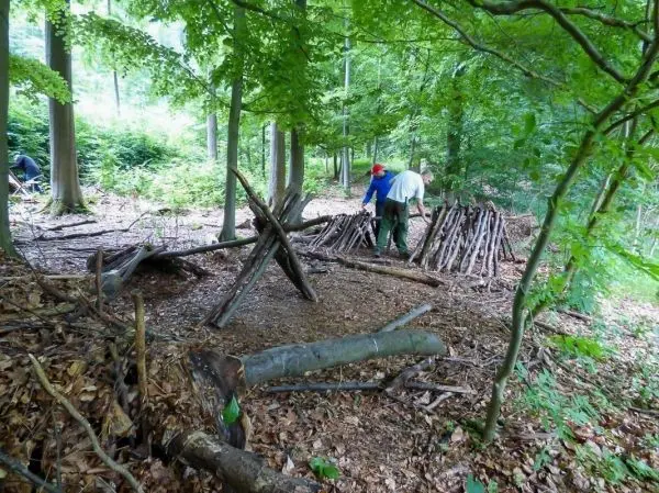 Zwei Personen bauen eine Holzstruktur im Wald aus Ästen und Stämmen
