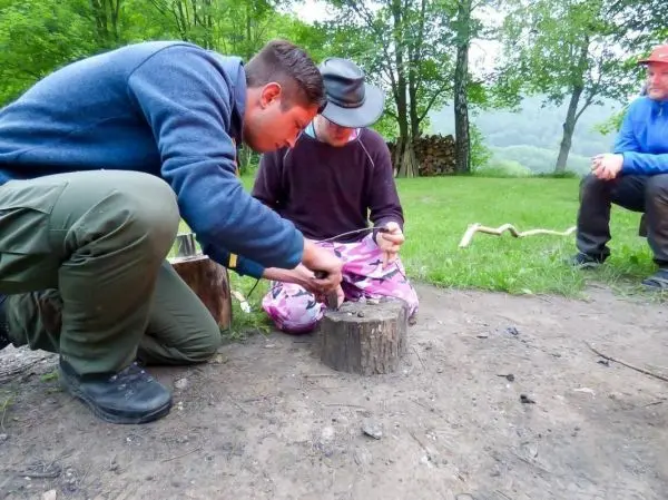 Zwei Personen entzünden Zunder mit einem Feuerstahl auf einem Baumstumpf