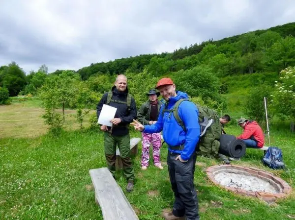 Zwei Personen mit Rucksäcken stehen an einem Lagerfeuerplatz in der Natur