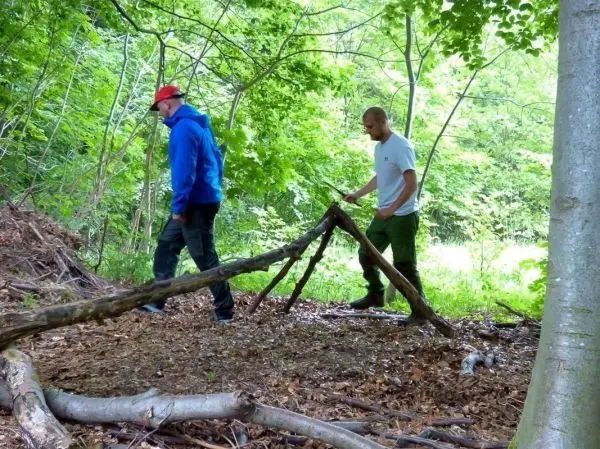 Zwei Personen prüfen eine selbstgebaute Holzkonstruktion im Wald