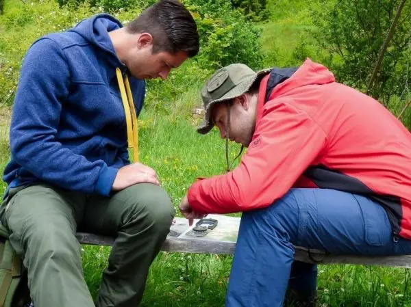 Zwei Personen studieren eine Karte und ein GPS-Gerät auf einer Holzbank