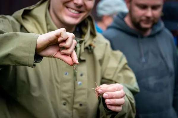 Angler hält Köder in der Hand und zeigt ihn einer Gruppe