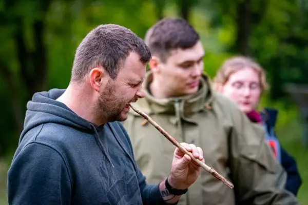 Ein Mann bläst in einen Stock, während andere zuschauen