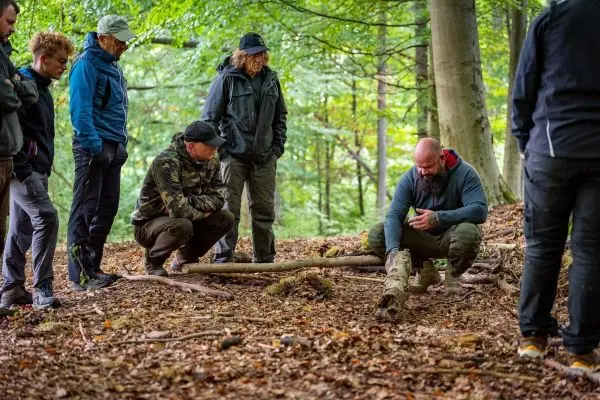 Ein Mann demonstriert Holzarbeit mit einem Stock, während andere zuschauen