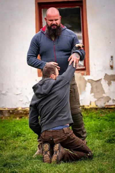 Ein Mann kniet und greift nach dem Arm eines stehenden Mannes