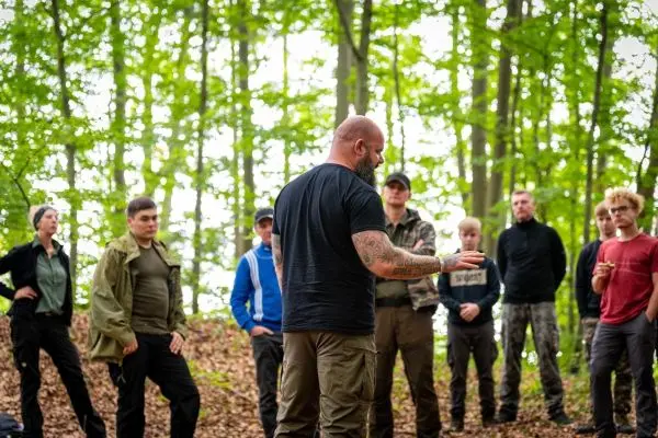 Ein Trainer erklärt Techniken in einem Wald mit Teilnehmern im Hintergrund
