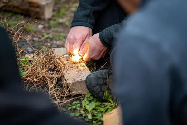 Feuerstahl erzeugt Funken auf Zunder in einer Holzunterlage