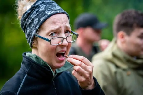 Frau mit Brille hält ein Insekt zwischen den Fingern und schaut überrascht