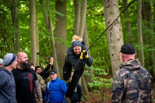 Frau überquert selbstgebaute Seilbrücke zwischen Bäumen im Wald