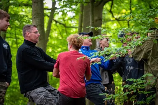 Gruppe zieht an einem Seil zwischen Bäumen im Wald