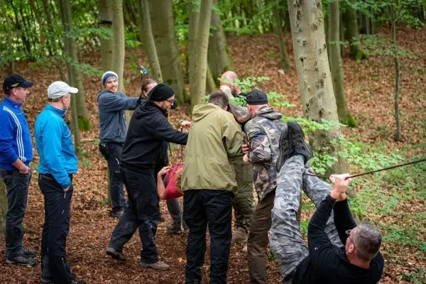 Gruppenteilnehmer üben eine Seilquerung zwischen Bäumen im Wald