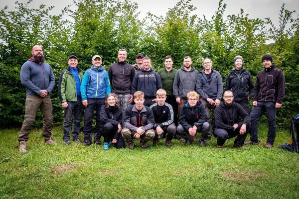 Gruppierung von Personen in Outdoor-Bekleidung auf einer Wiese vor Sträuchern
