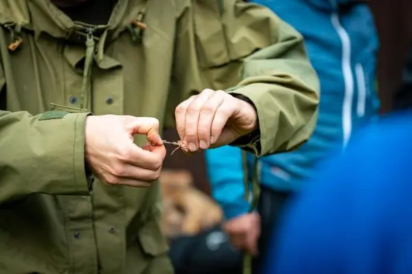 Hände binden eine Schnur zu einem Knoten in einer grünen Jacke