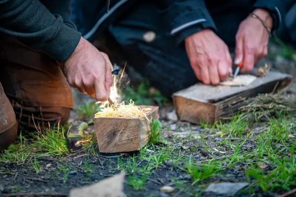 Hände erzeugen Funken auf Holzstück beim Feuer machen