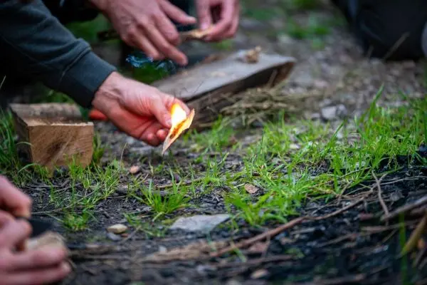 Hand hält brennendes Stück Holz über den Boden beim Feuer machen