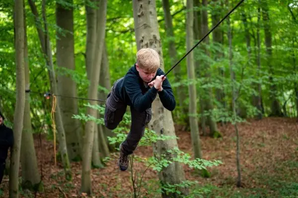 Junge schwingt an einem Seil zwischen Bäumen im Wald