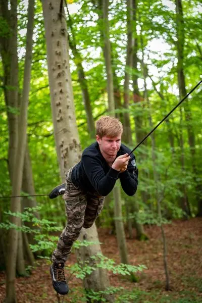 Junge schwingt an einem Seil zwischen Bäumen im Wald