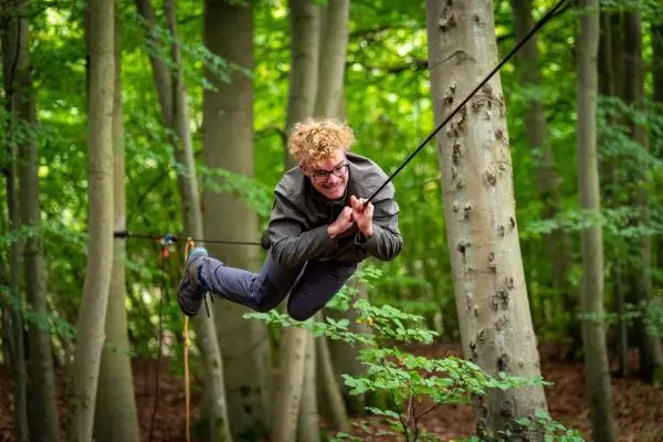 Junge schwingt an einer Seilbrücke zwischen Bäumen im Wald