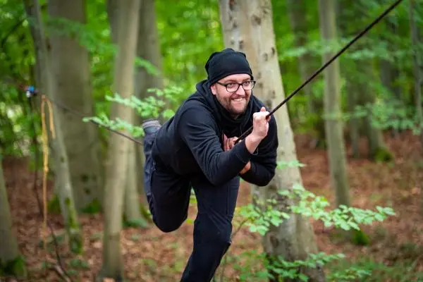 Mann balanciert auf einer gespannten Schnur zwischen Bäumen im Wald