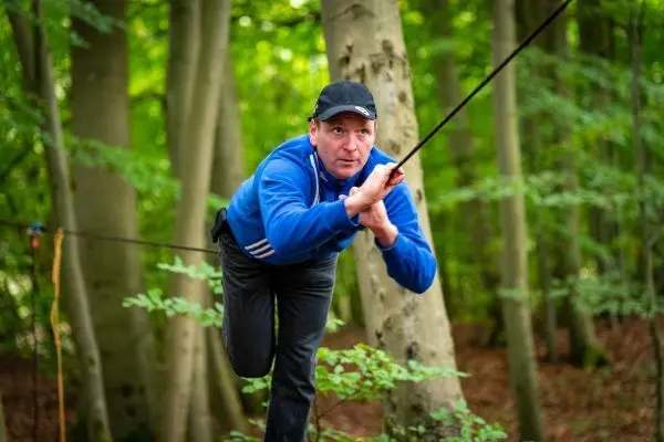 Mann balanciert auf einer Seilbrücke zwischen Bäumen im Wald