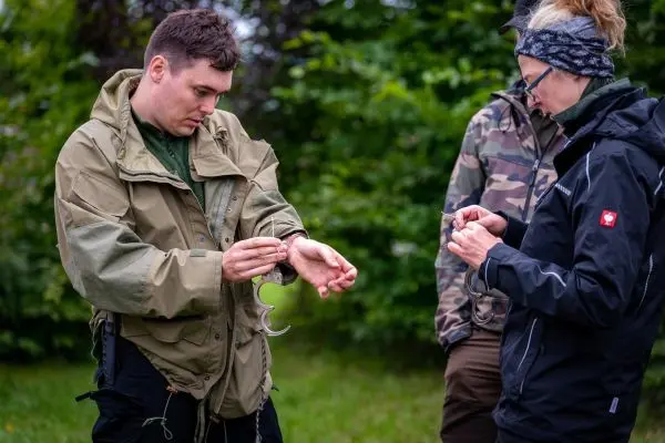 Mann befestigt eine Handschelle an seinem Handgelenk, während andere zuschauen