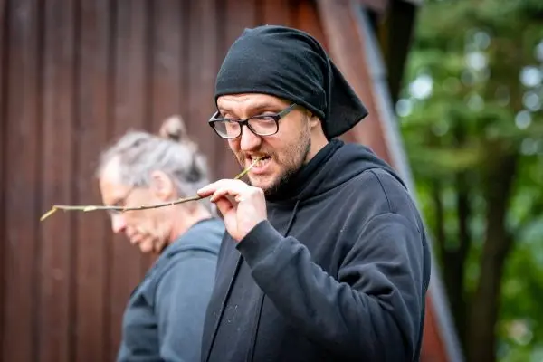 Mann kaut auf einem Zweig und trägt eine schwarze Kopfbedeckung