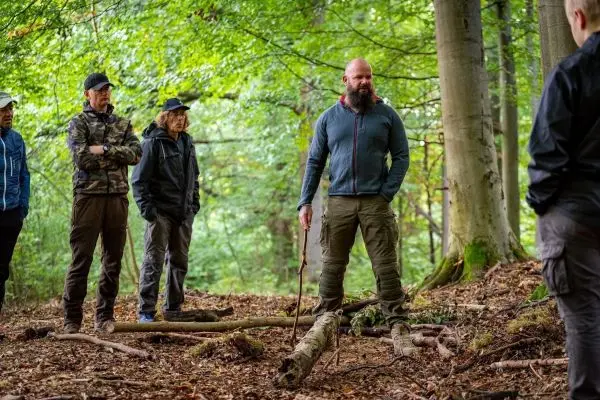 Mann mit Stock erklärt Technik in einem Wald, umgeben von Zuhörern